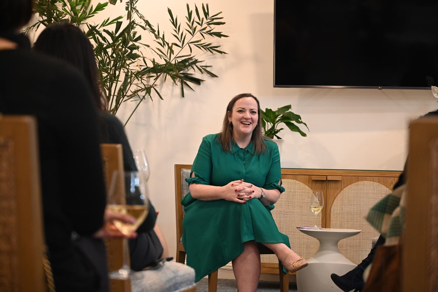Leslie Feinzaig in a green dress, seated and speaking with people gathered around her