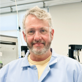 Lewis Dutel wearing safety glasses and a light-blue lab coat in a laboratory