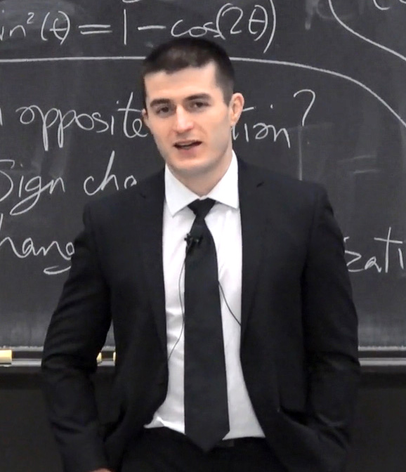 Lex Fridman speaking in front of a chalkboard covered in mathematical notation