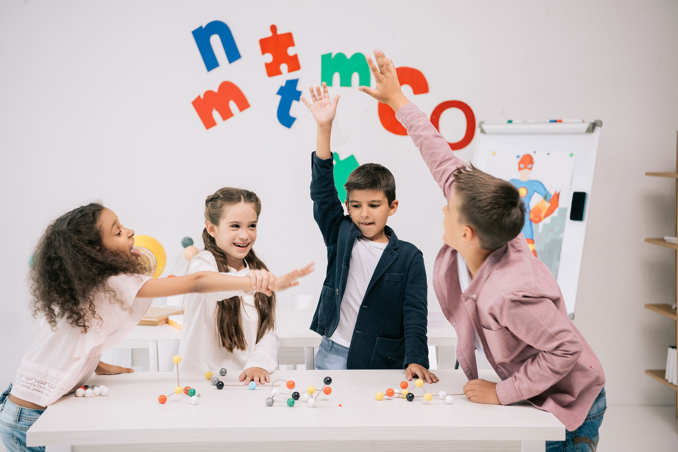 Children raising their hands around a classroom activity table