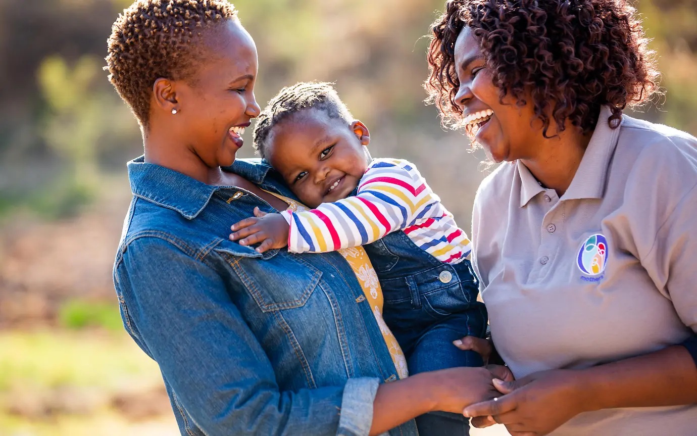 A mothers2mothers worker talking with a woman holding a young child