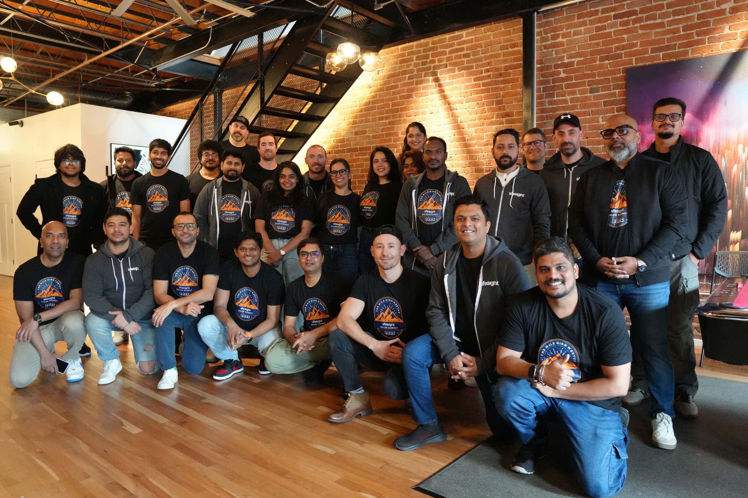 Lifesight colleagues gathered in matching sales summit shirts in a brick-walled room