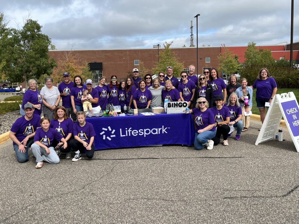 Lifespark employees gathered in purple shirts around a picnic table outdoors