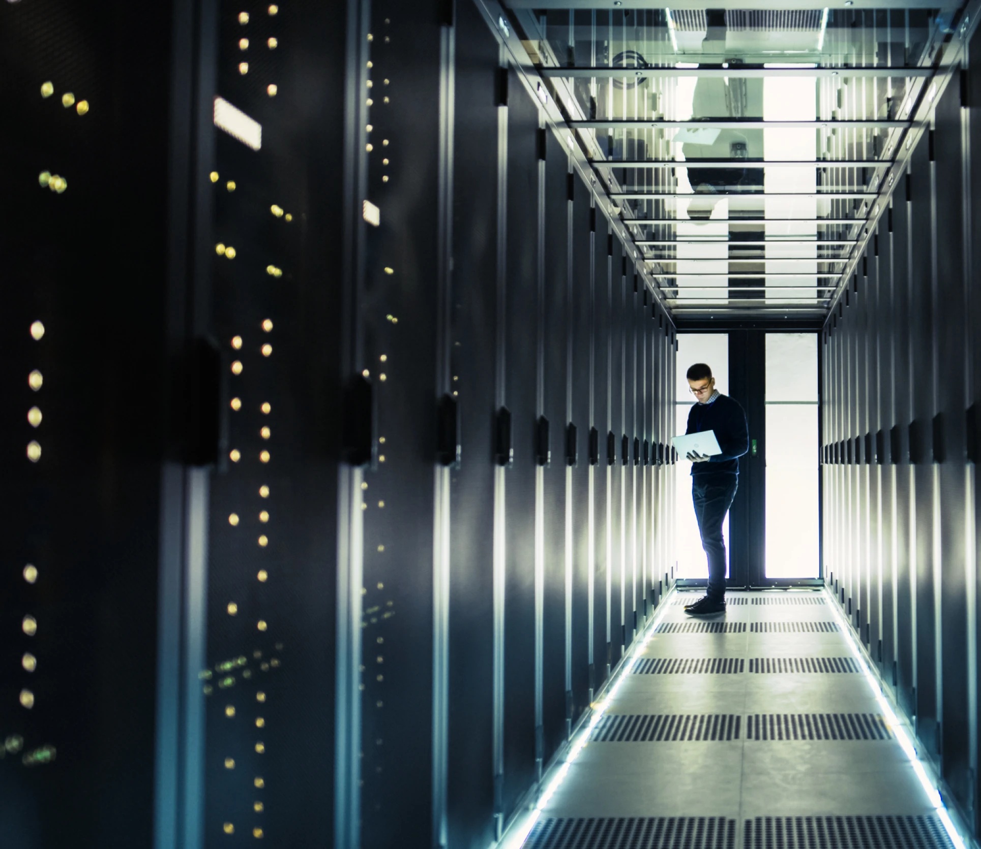An engineer with a laptop between rows of server cabinets