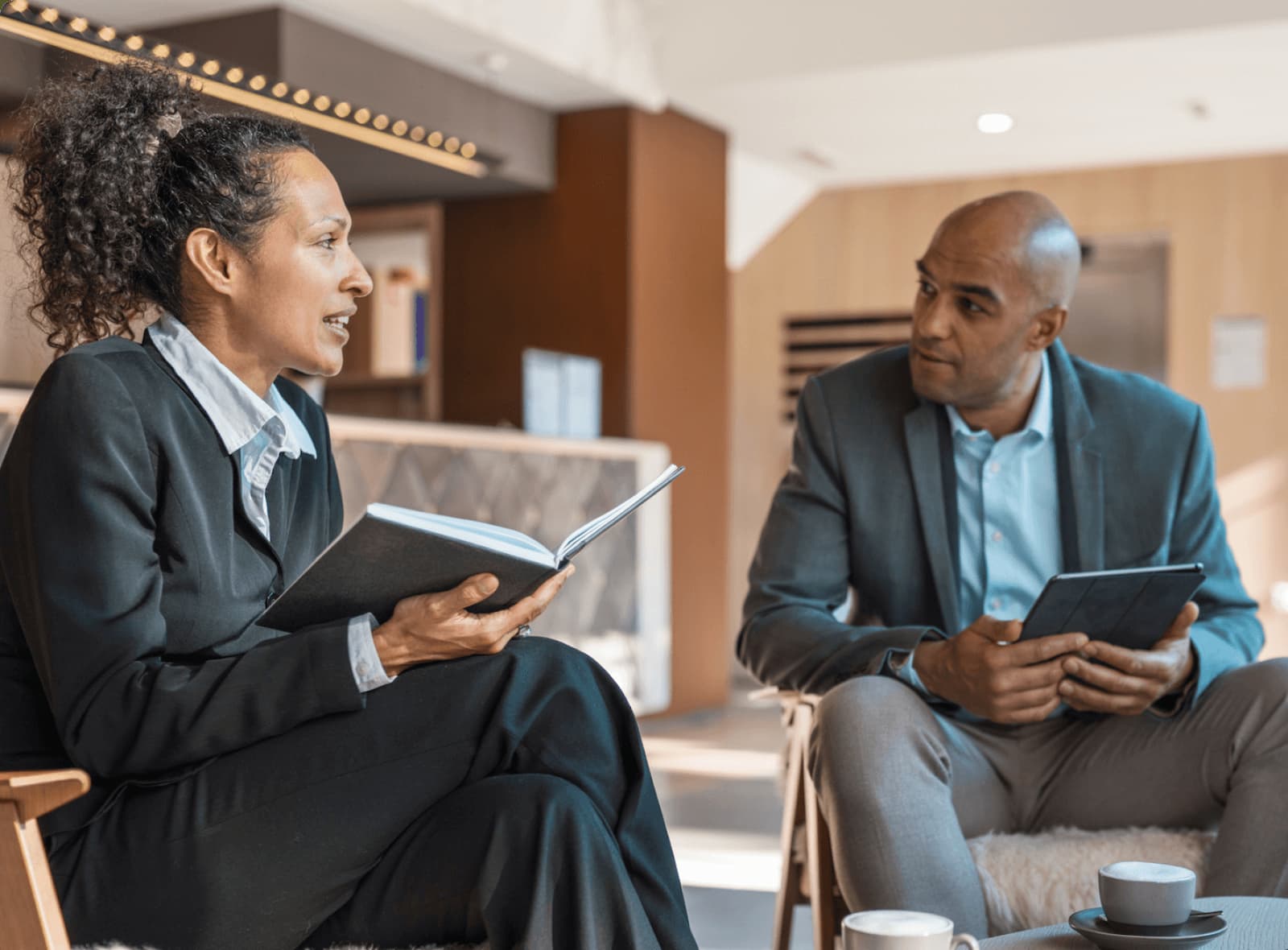 Two hospitality professionals talking with a notebook and tablet in a hotel lounge