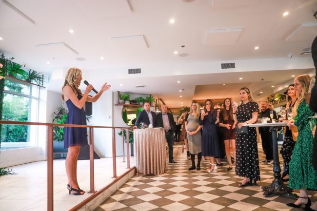 Lindsay Nahmiache speaking into a microphone to a standing audience at an event