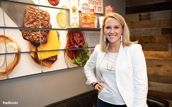 Lindsay Radkoski standing inside a Wendy's restaurant beside a wall display of menu photography