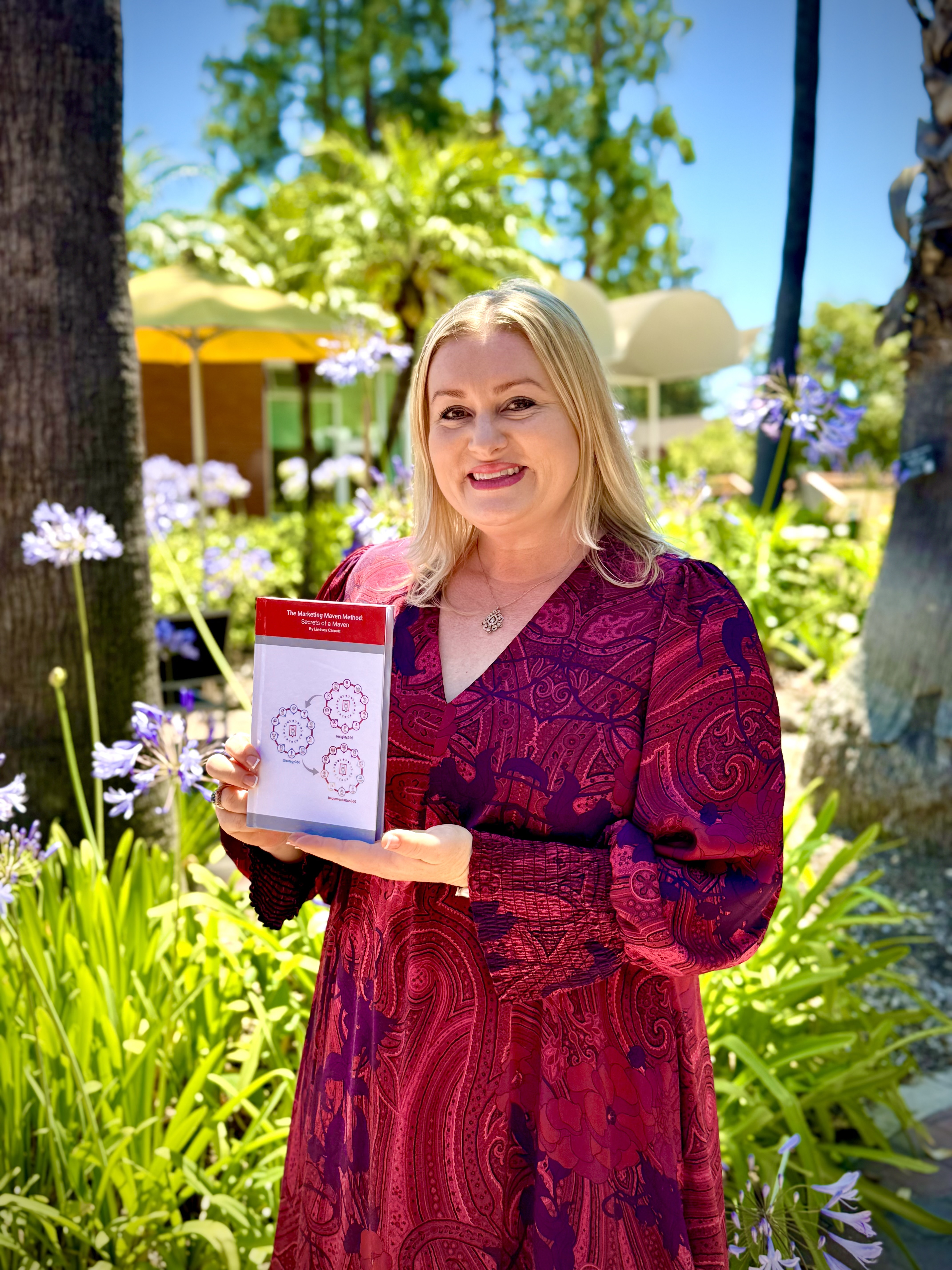 Lindsey Carnett outdoors holding her book The Marketing Maven Method: Secrets of a Maven