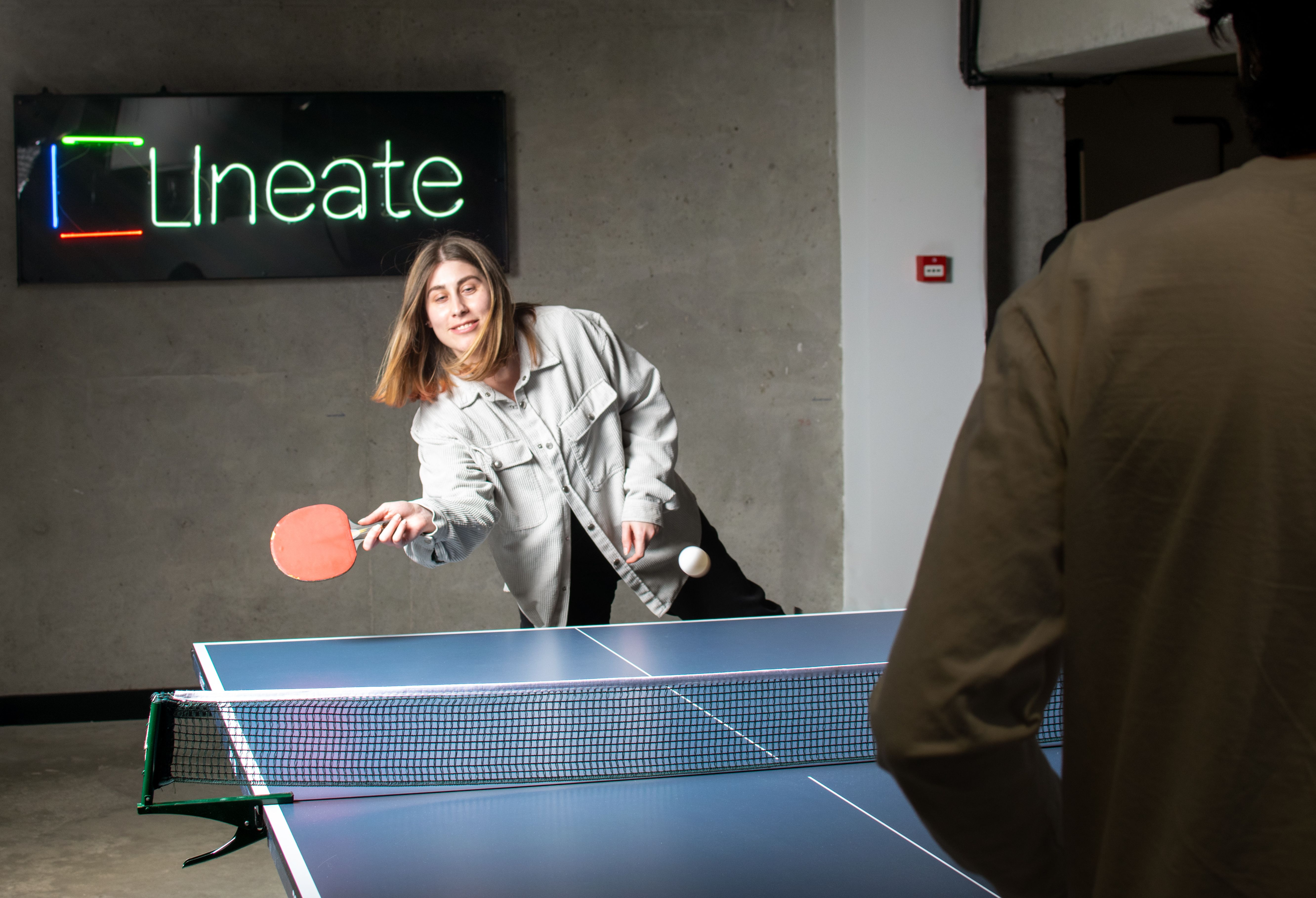 Two people playing table tennis beneath a Lineate sign in the company gallery
