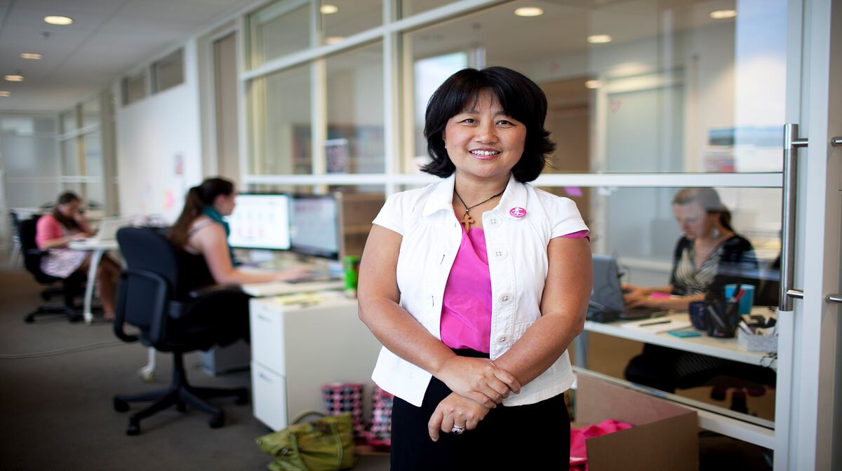 Ling Chai standing in a Boston office, with colleagues working at computers behind her