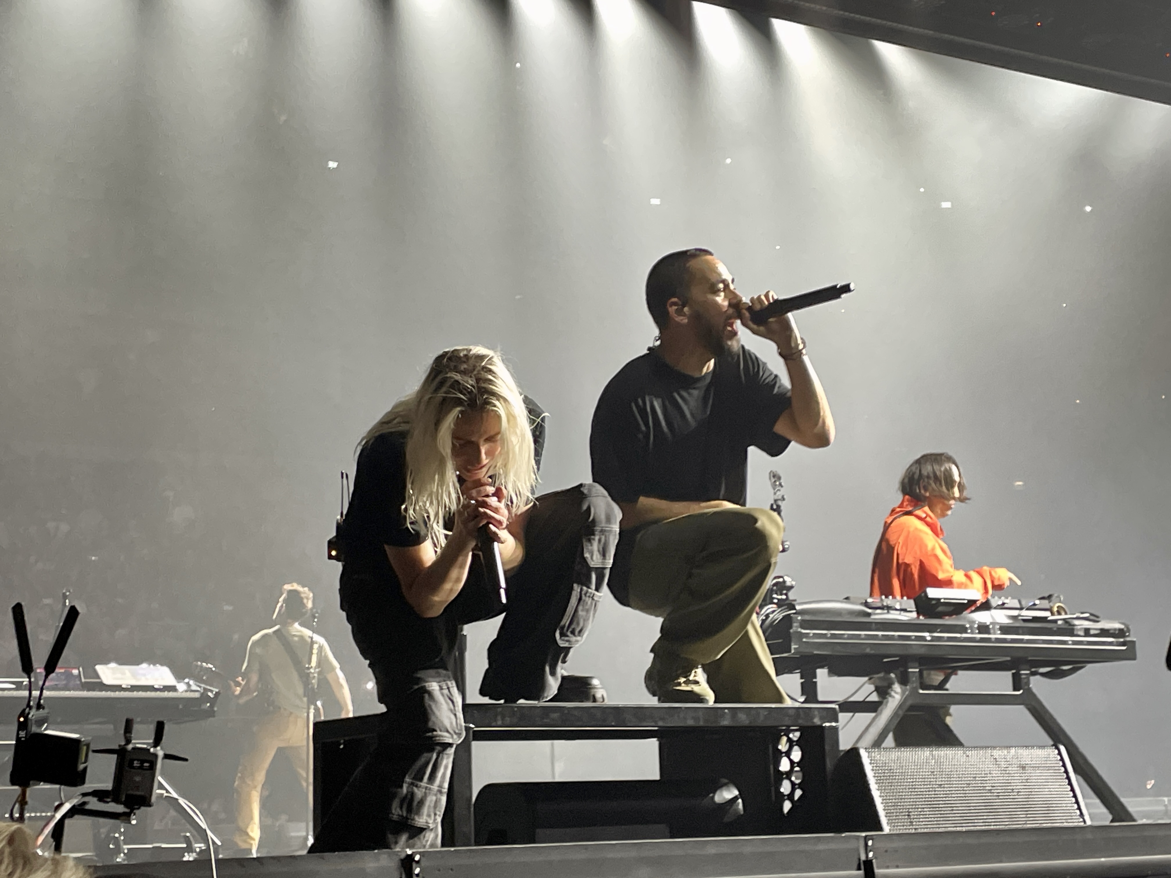Emily Armstrong and Mike Shinoda crouch at the front of the O2 Arena stage while Joe Hahn performs behind them