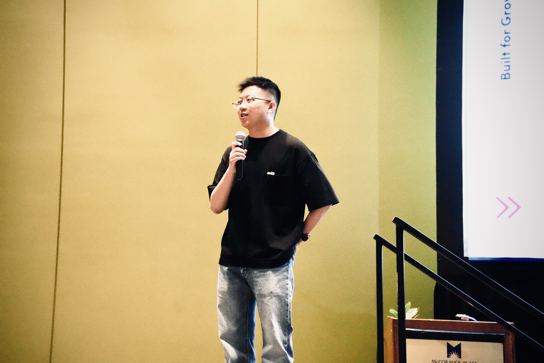 Linxin Wen speaking onstage with a handheld microphone