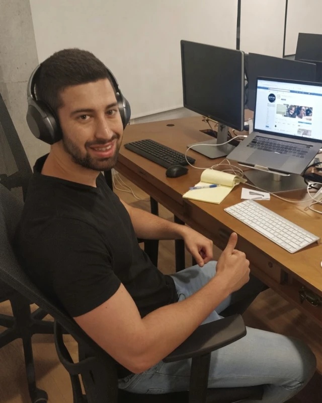 Lior Pozin seated at a desk with a laptop and monitor
