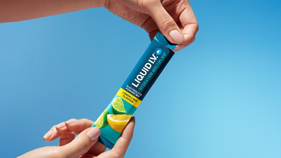 Hands tearing open a Lemon Lime Liquid I.V. electrolyte powder stick against a blue background