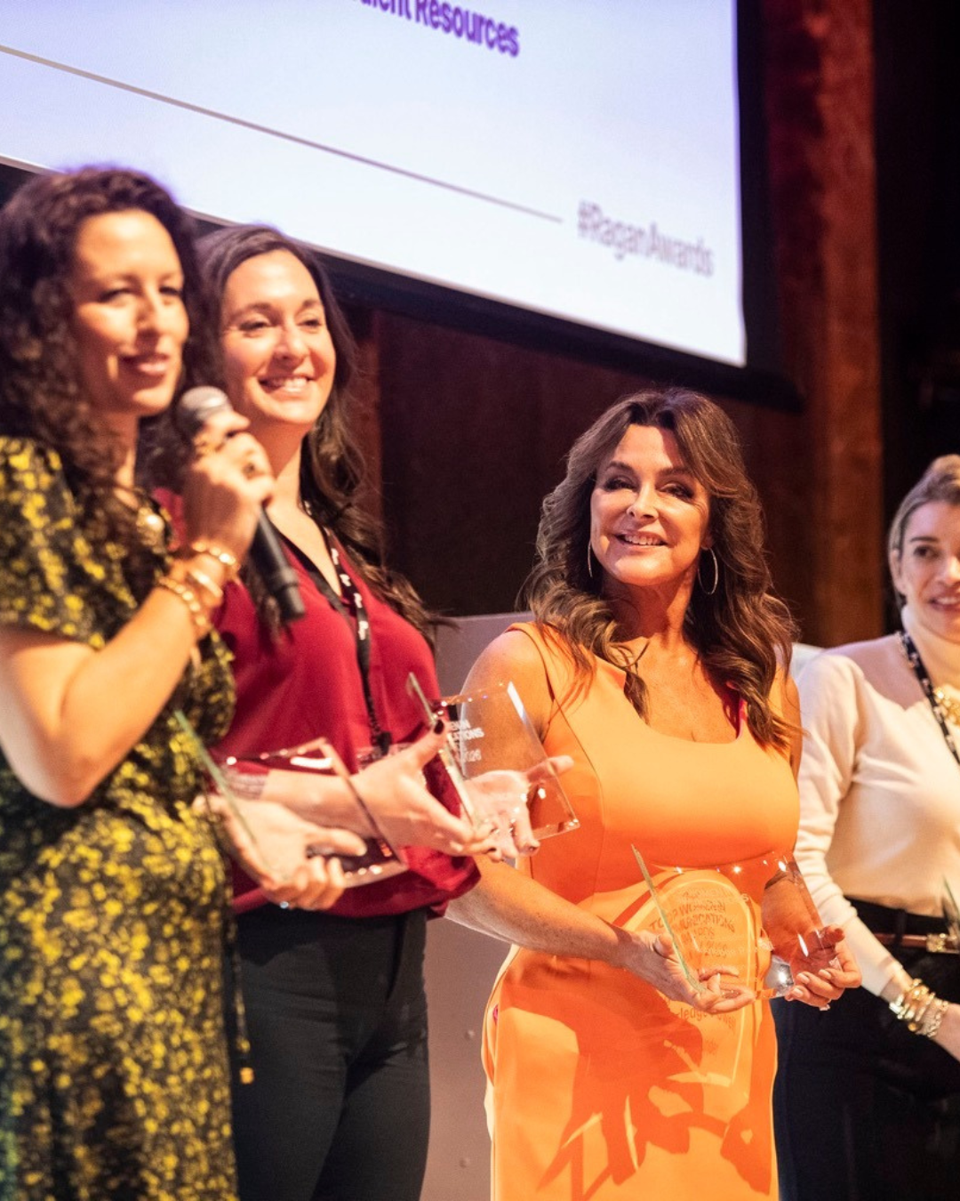 Lisa Arledge Powell in an orange dress holding her award alongside fellow honorees