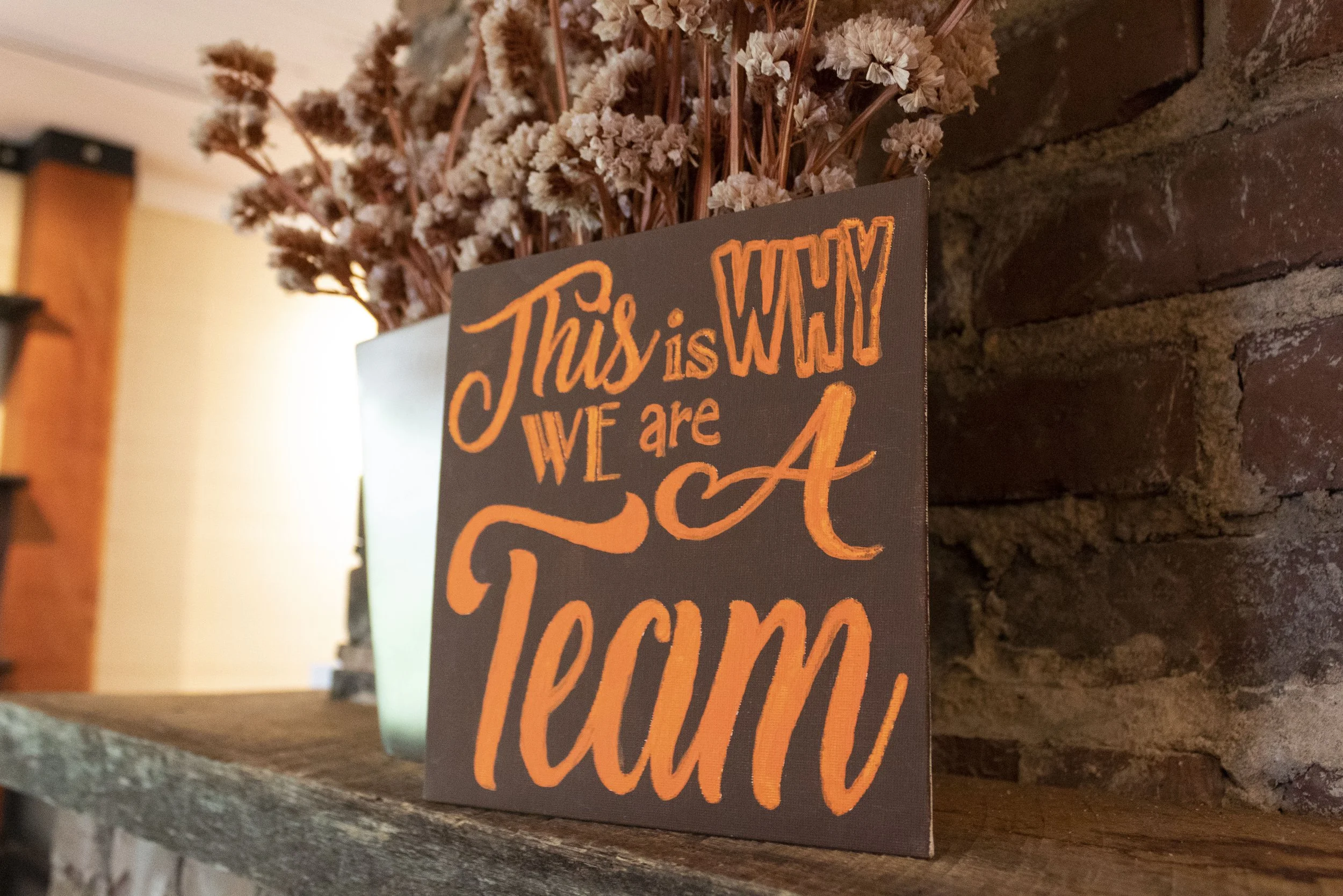 A sign reading This is why we are a team on a brick fireplace mantel at Full Tilt