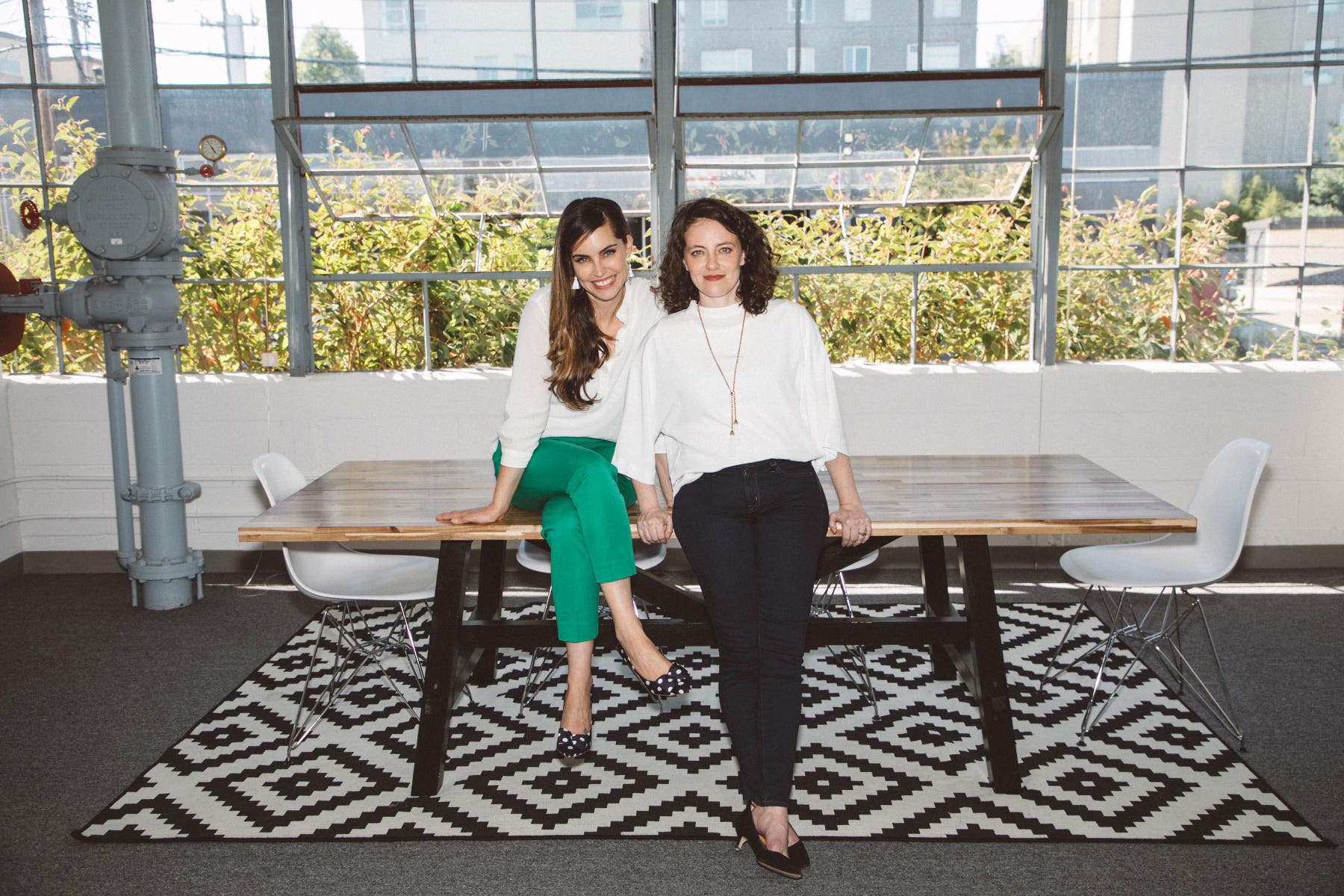 Robin McIntosh, left, and Lisa McLaughlin, right, sitting on a table in a sunlit workspace