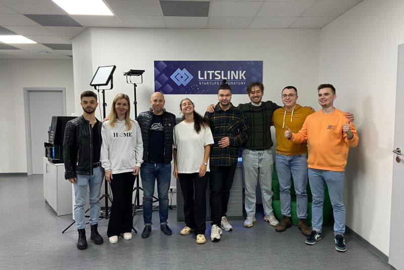 Eight LITSLINK colleagues standing together in an office beneath the company’s Startups Laboratory wall sign