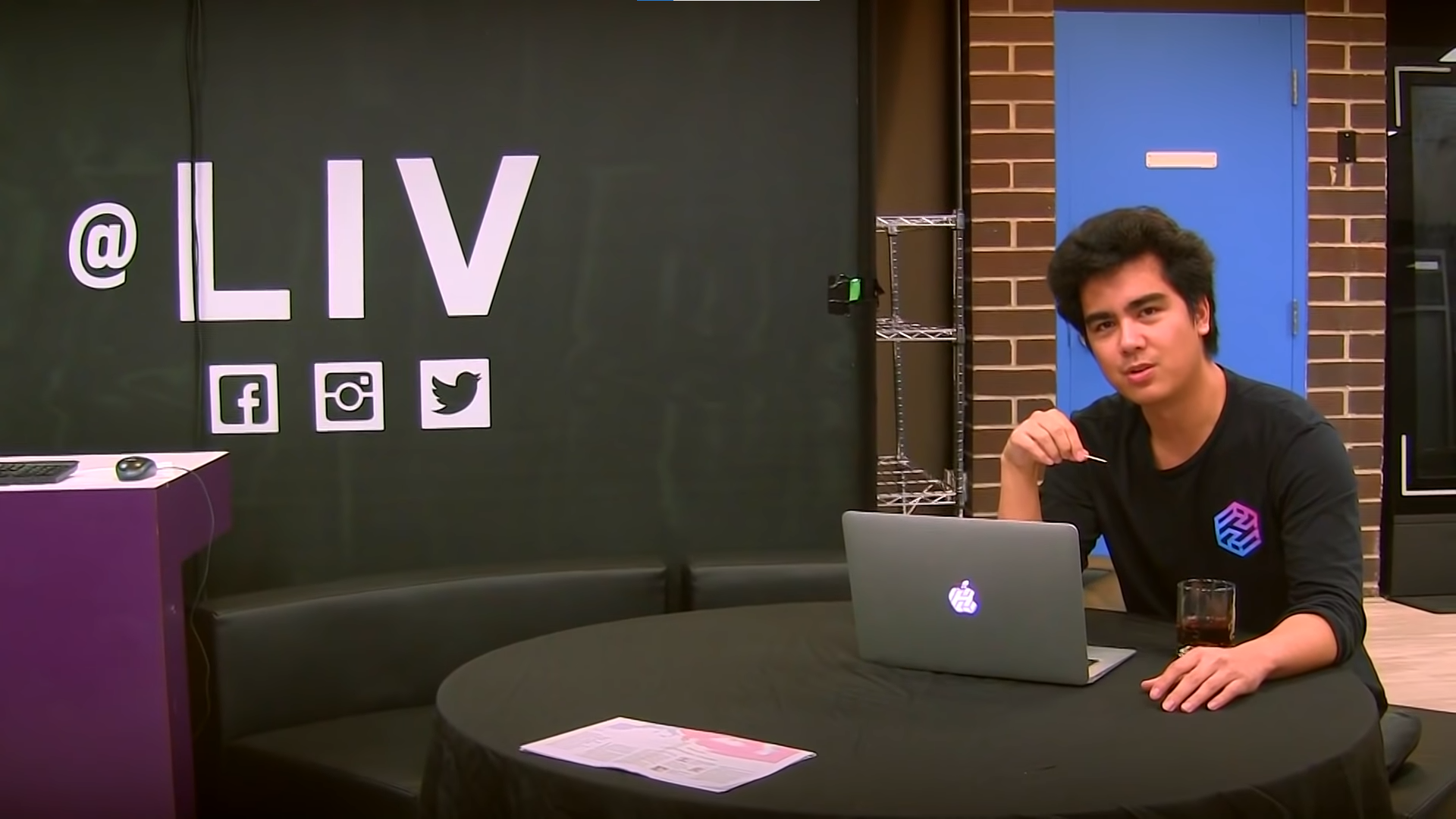 An early LIV workspace with a presenter seated beside the LIV name on a black wall