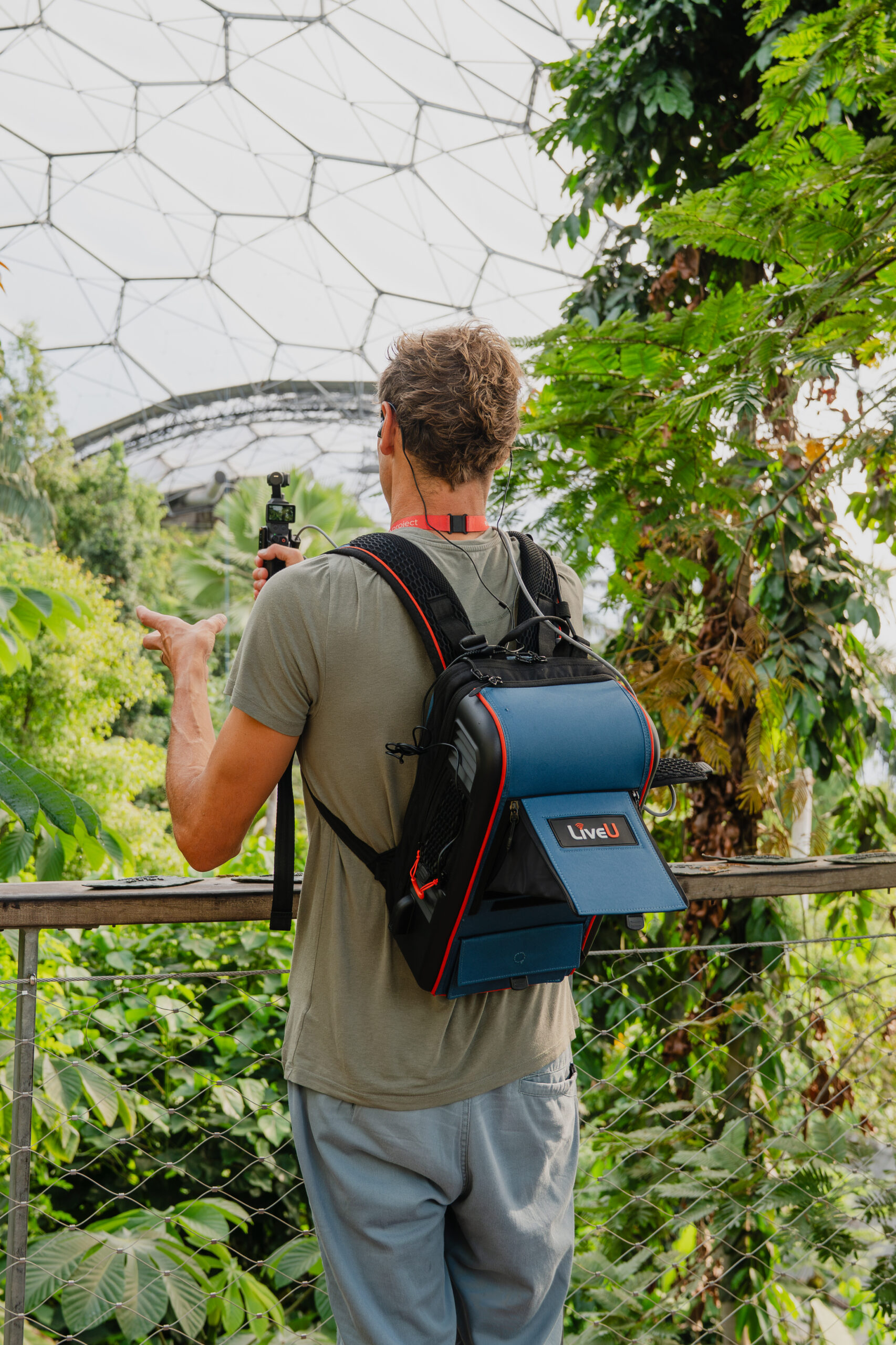 An Eden Project presenter carrying a LiveU backpack while filming inside a planted biome