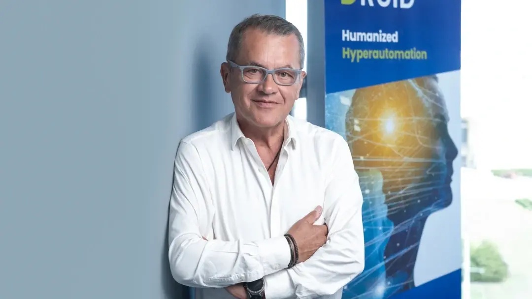 Liviu Dragan in a white shirt and glasses beside a DRUID banner