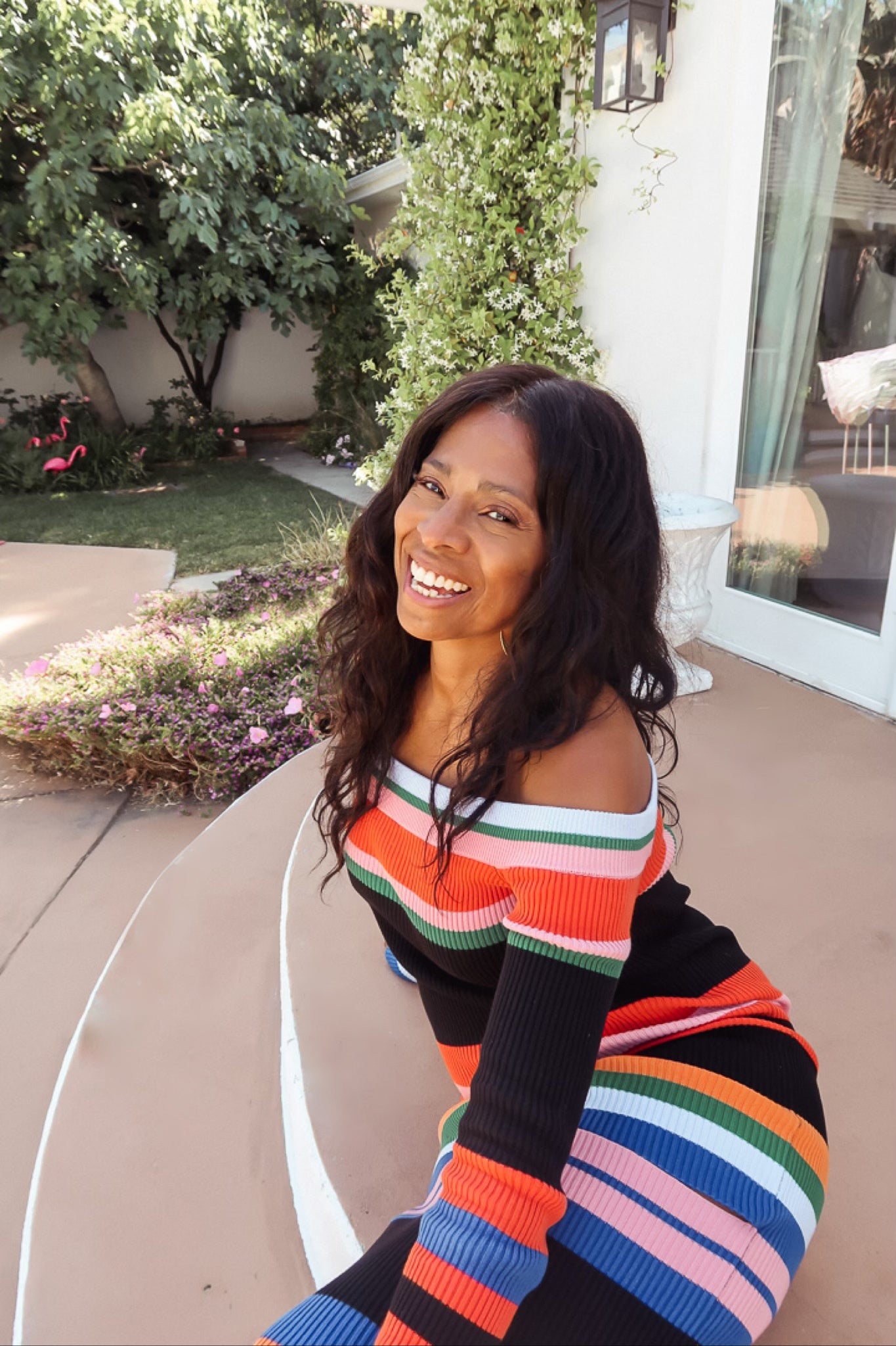 Liza Vassell smiling outdoors beside a garden, wearing a colorful striped dress