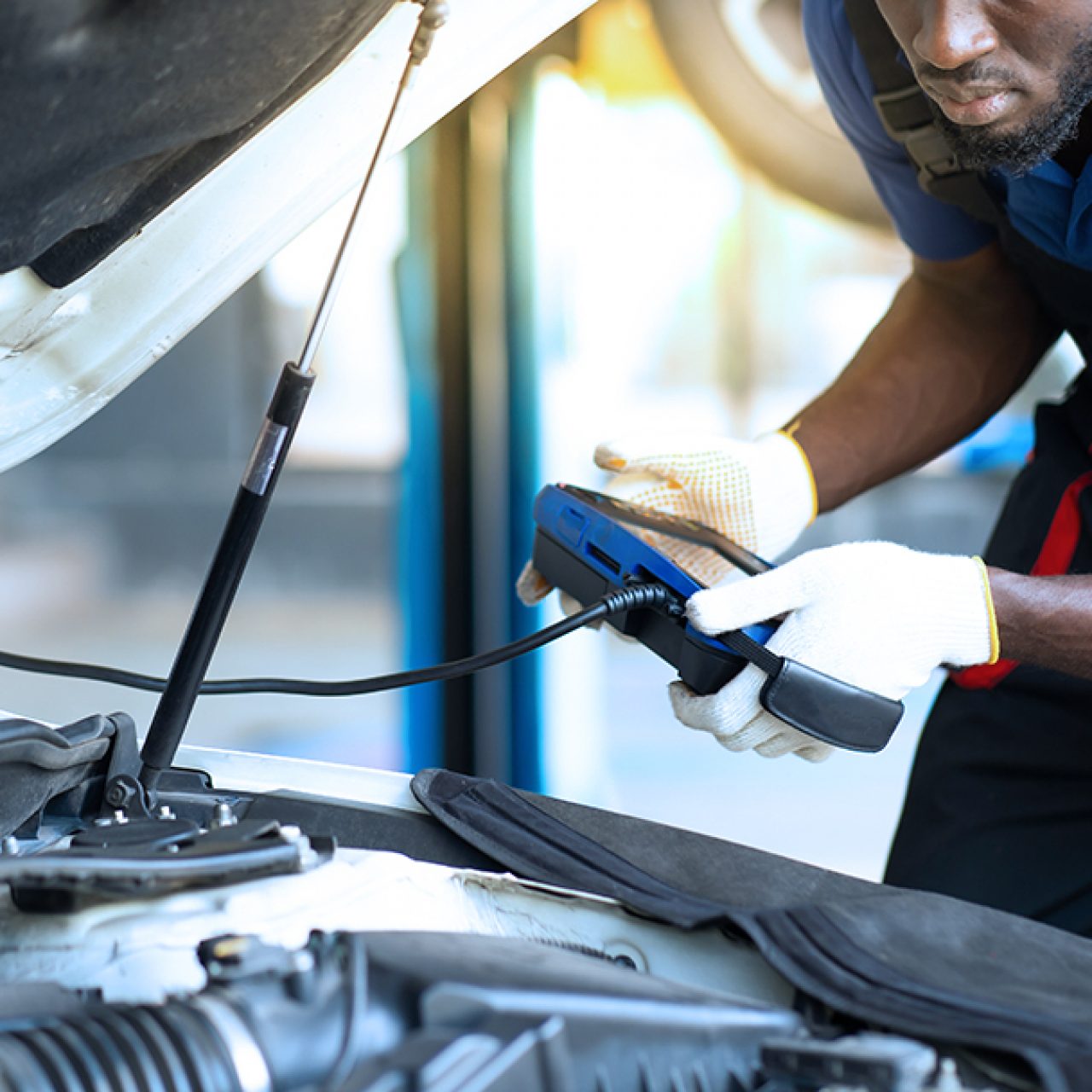 Technician using diagnostic equipment beside an open vehicle hood