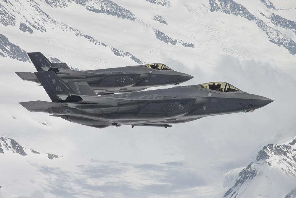 Two gray F-35 fighters in formation over snow-covered mountains