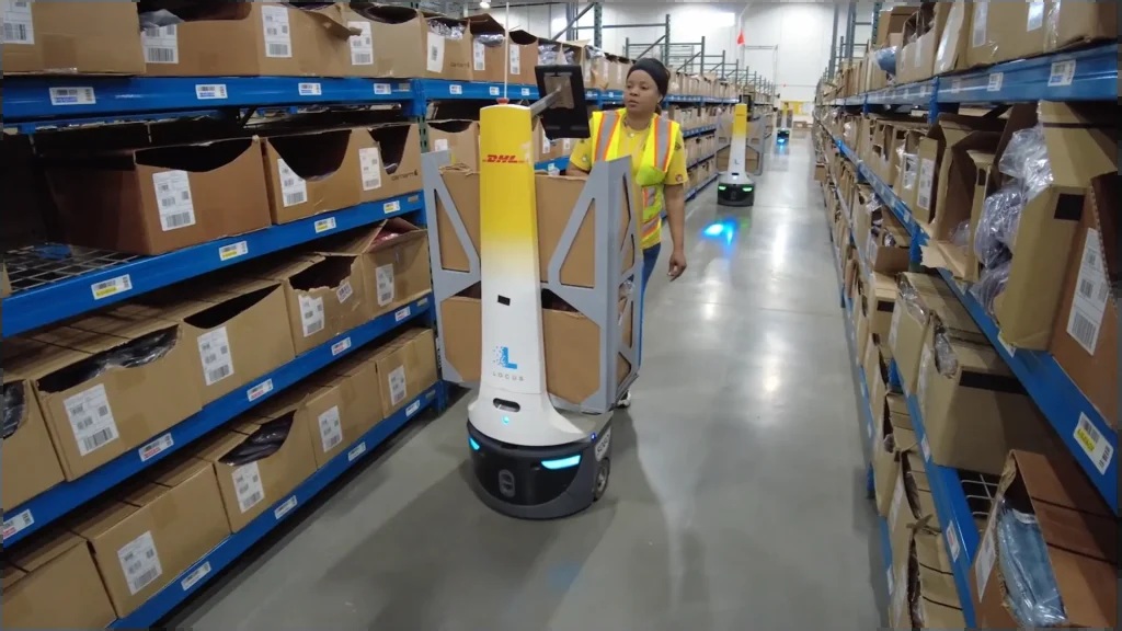 A warehouse associate beside a Locus robot carrying cartons at a DHL Carhartt operation