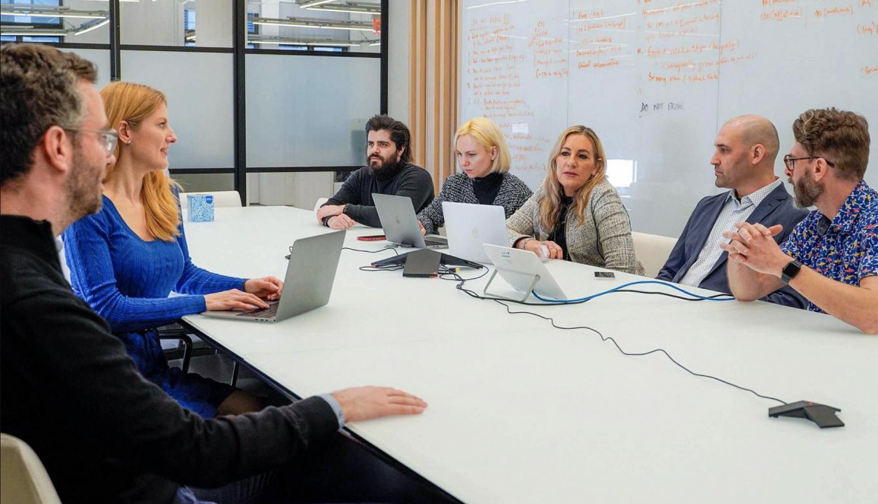 People with laptops meeting around a table, as pictured in BRINK’s Lohika case study