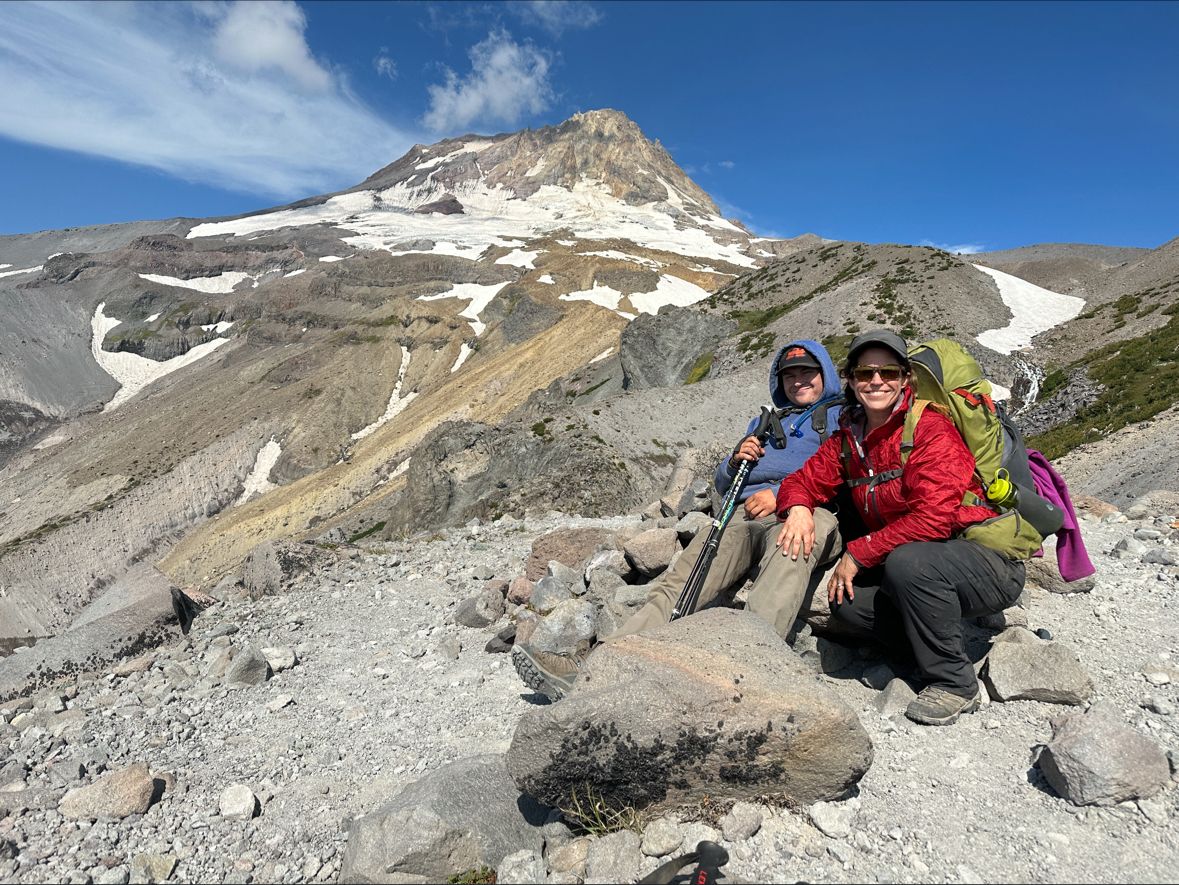 Londonne Corder and her son Gavin resting on the rocky Timberline Trail with Mount Hood behind them