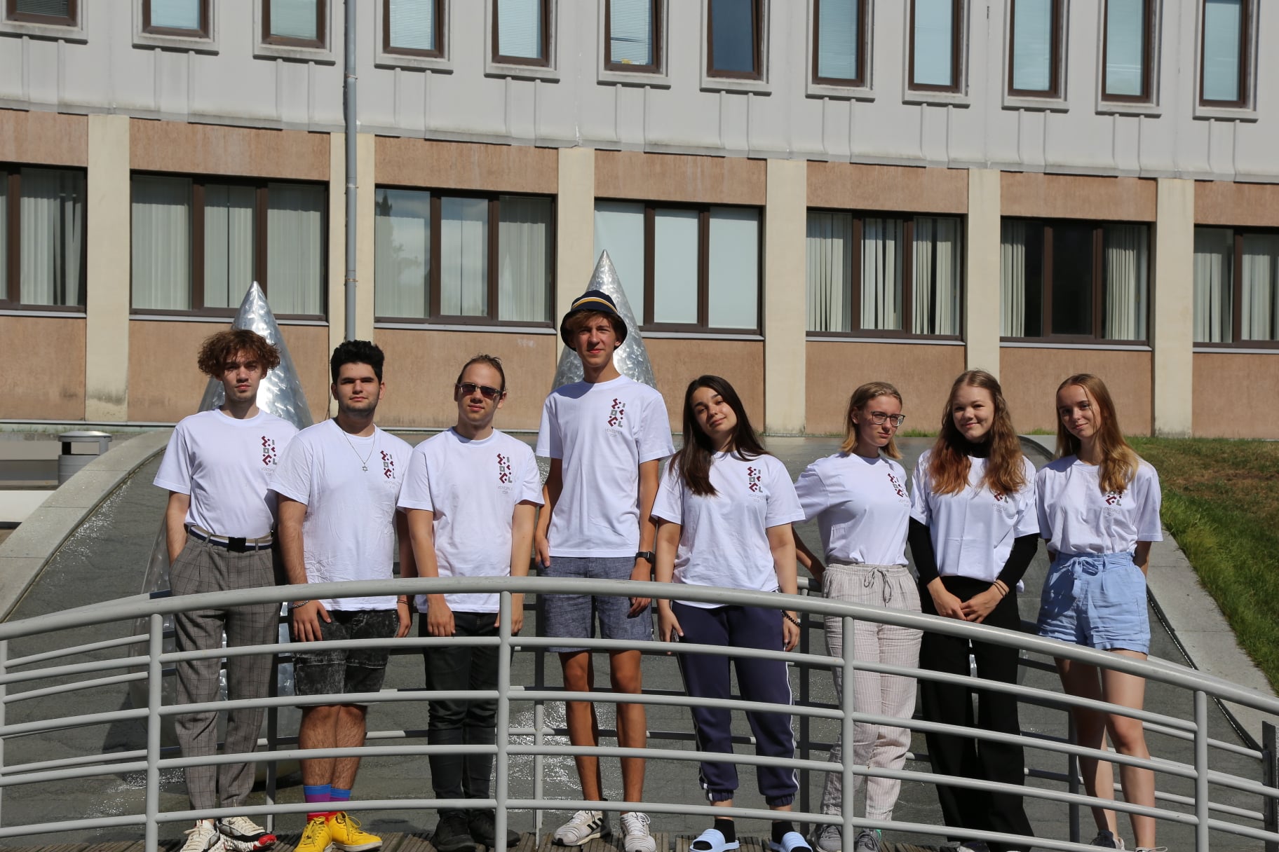 Eight members of Team Latvia at the 2021 International Linguistics Olympiad stand together outdoors in white team shirts
