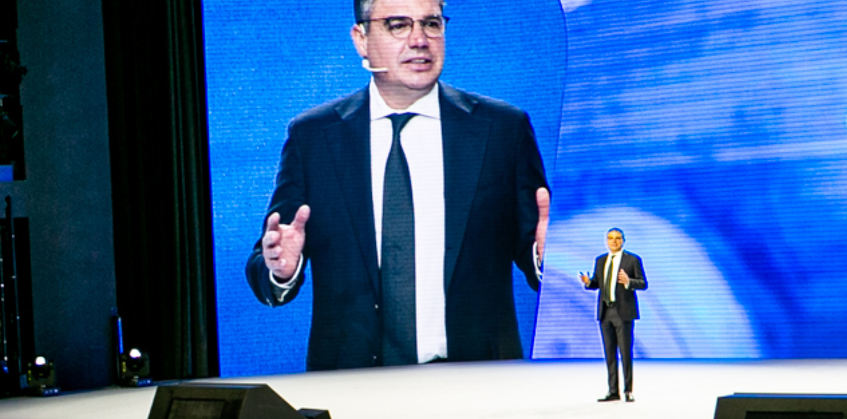 Lorenzo Simonelli speaking onstage beside a large projection of himself at the Baker Hughes Annual Meeting 2023