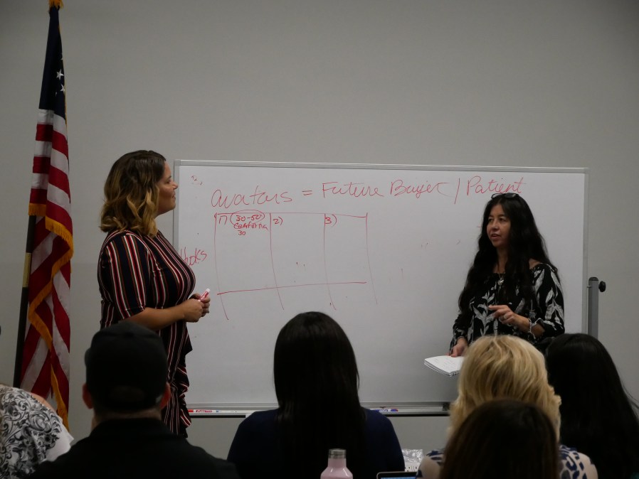 Lori Stinson beside a marketing instructor at a whiteboard during a workshop in Austin in 2019