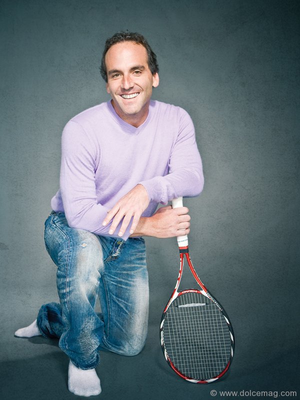 Lorne Abony kneeling with a tennis racket, wearing a lavender sweater, jeans and white socks