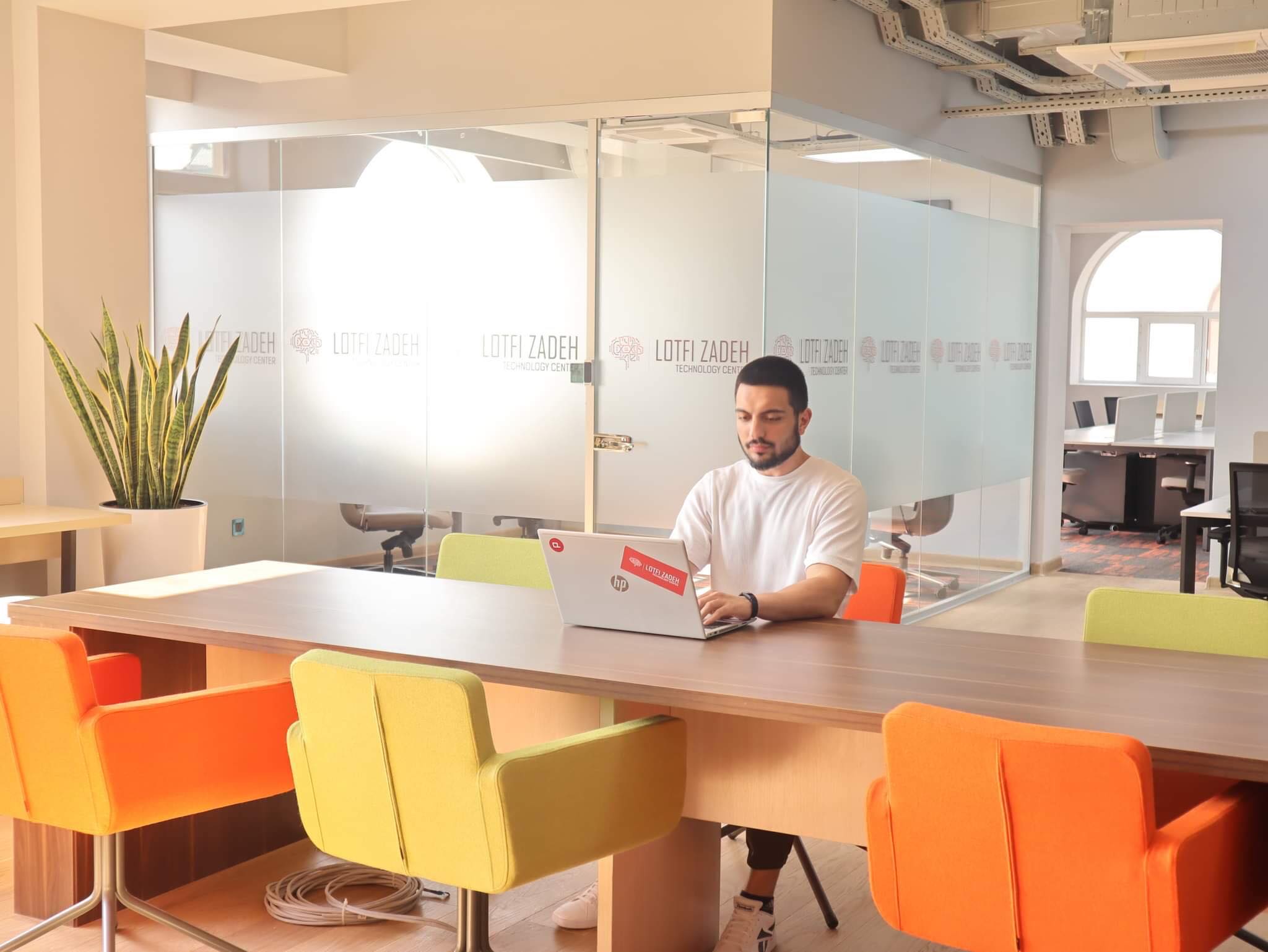 A person working at a laptop in an LTC shared area beside glass meeting rooms