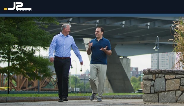 Lou LaRocca, on the right in a navy polo shirt, walking and talking with a colleague outdoors
