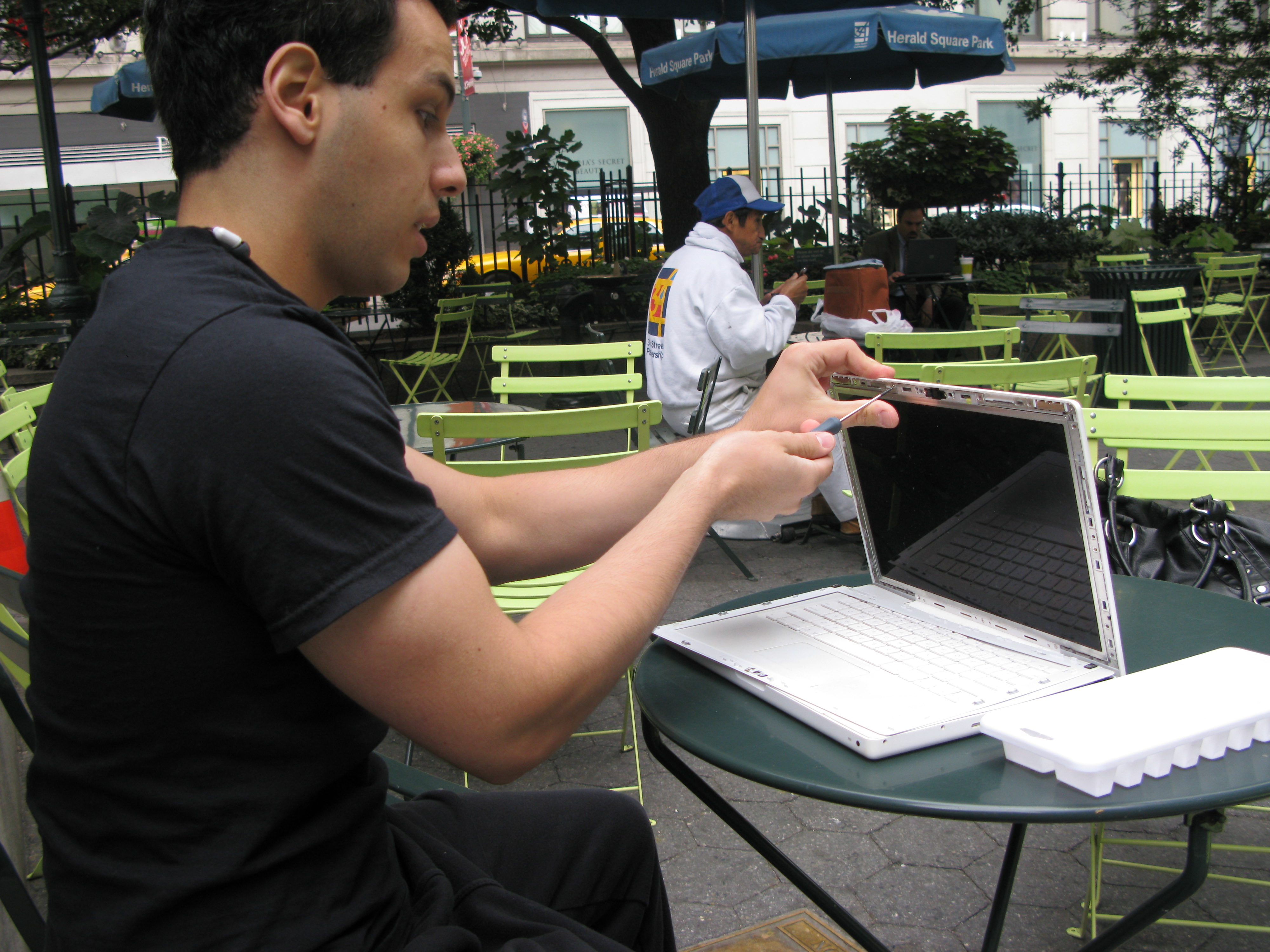 Louis Rossmann working on a white laptop at an outdoor table in Herald Square Park