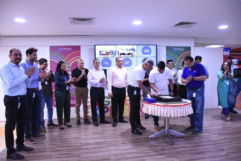 Cuelogic colleagues applaud as a cake is cut at an acquisition-anniversary celebration