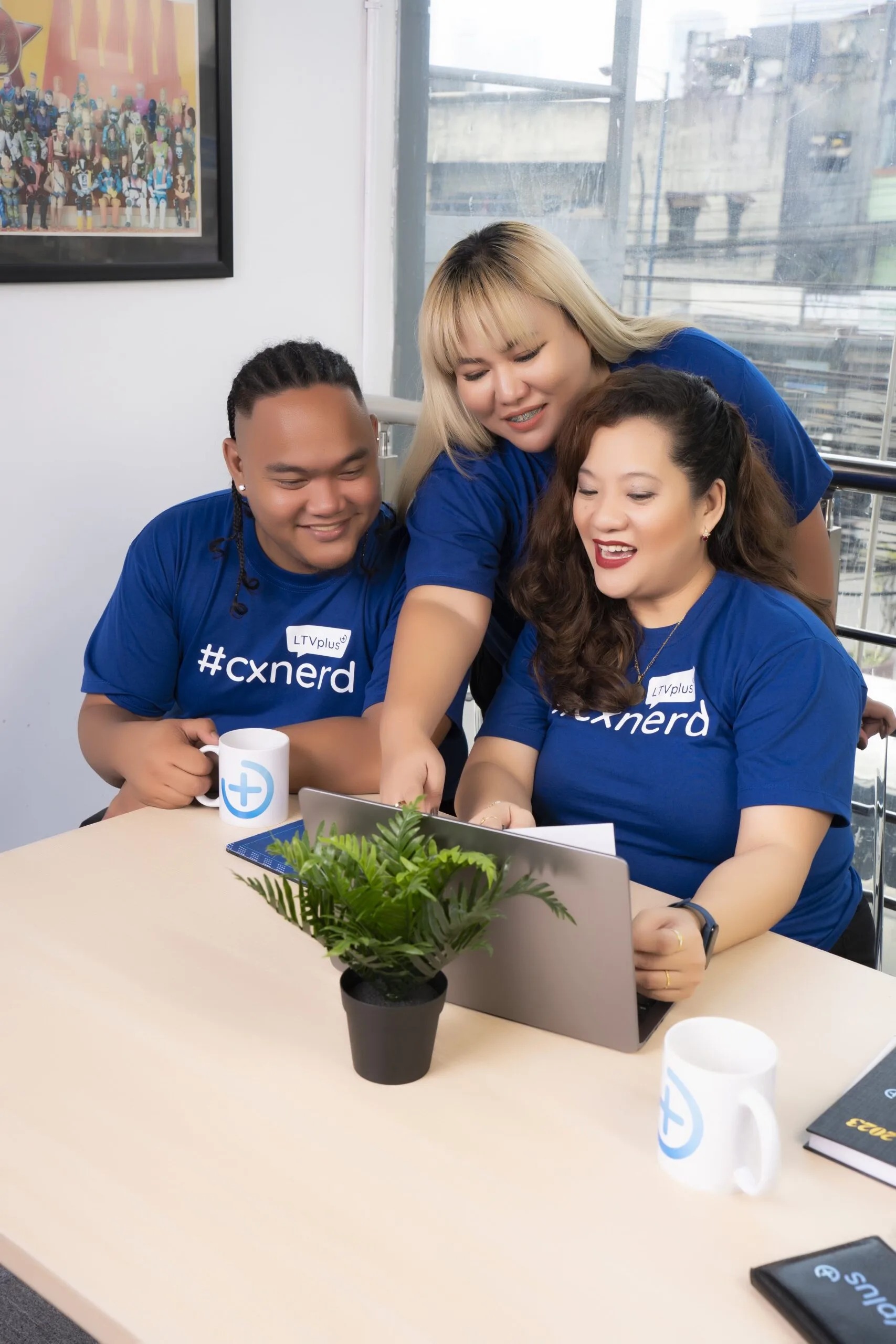 Three LTVplus team members in blue shirts gathered around a laptop