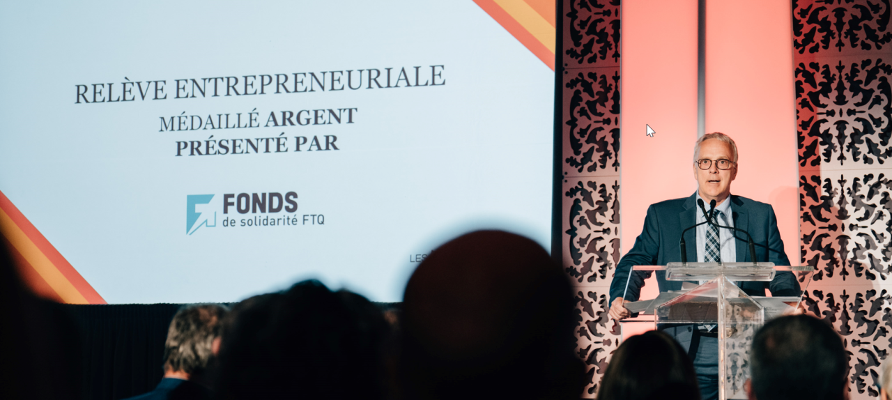 Luc Pinard at a lectern presenting the silver entrepreneurial succession award at Les Médaillés de la relève.