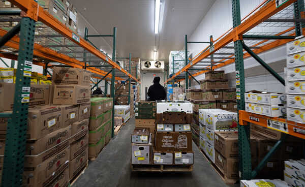 A warehouse worker beside a tall produce pallet built during a Jennifer-directed workflow