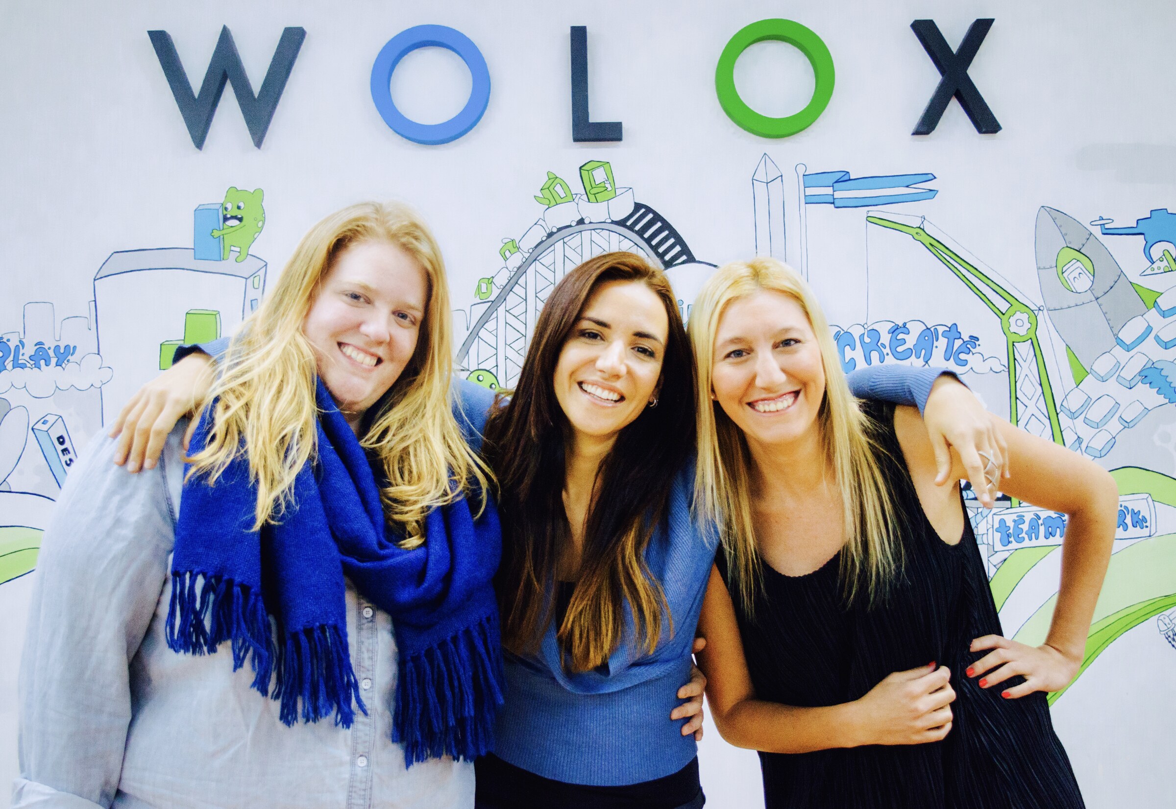 Luciana Reznik, at left, with two Wolox colleagues in front of a colorful Wolox mural