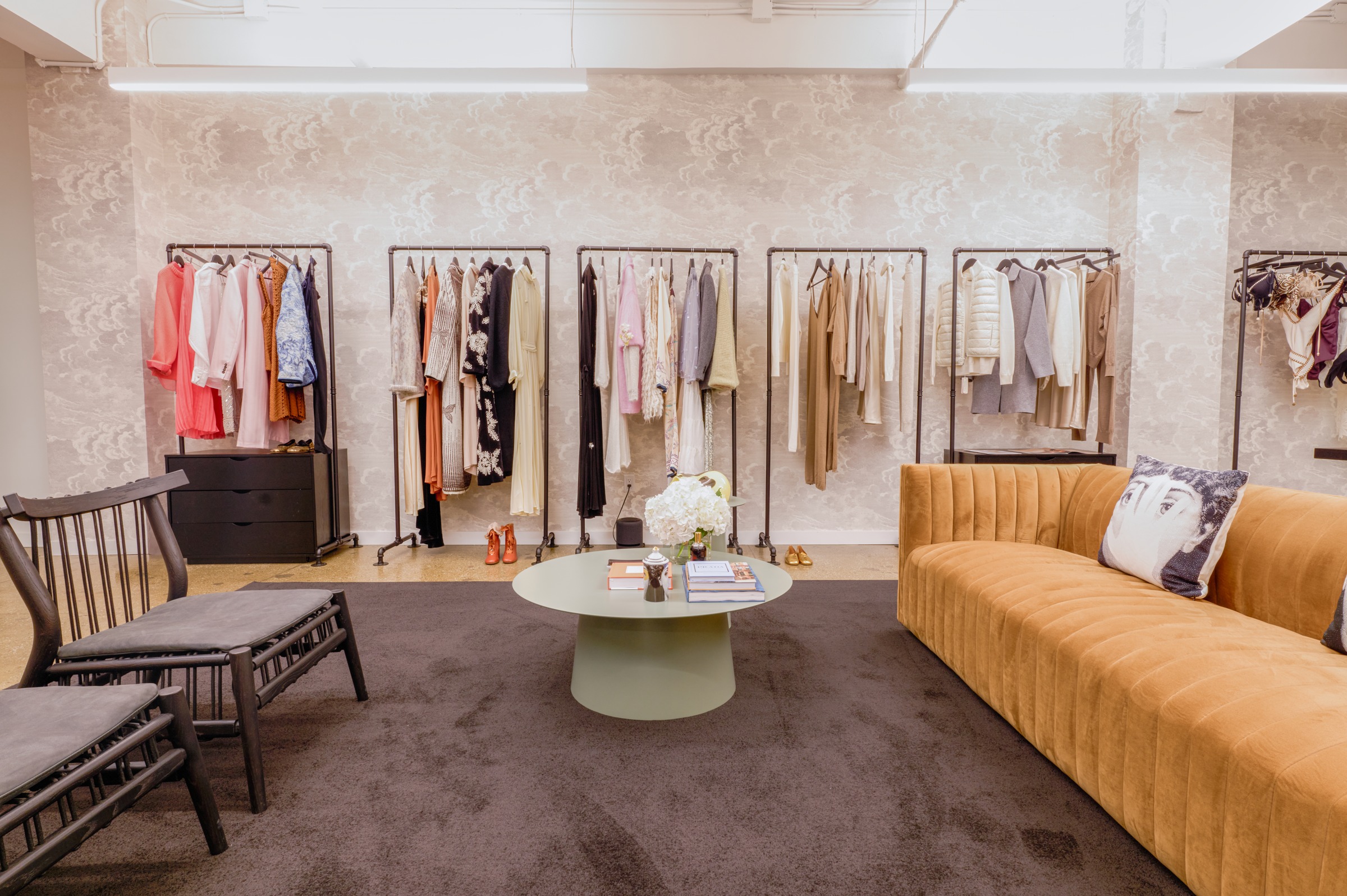LDR22's New York showroom with clothing rails, patterned walls, books and a curved ochre sofa