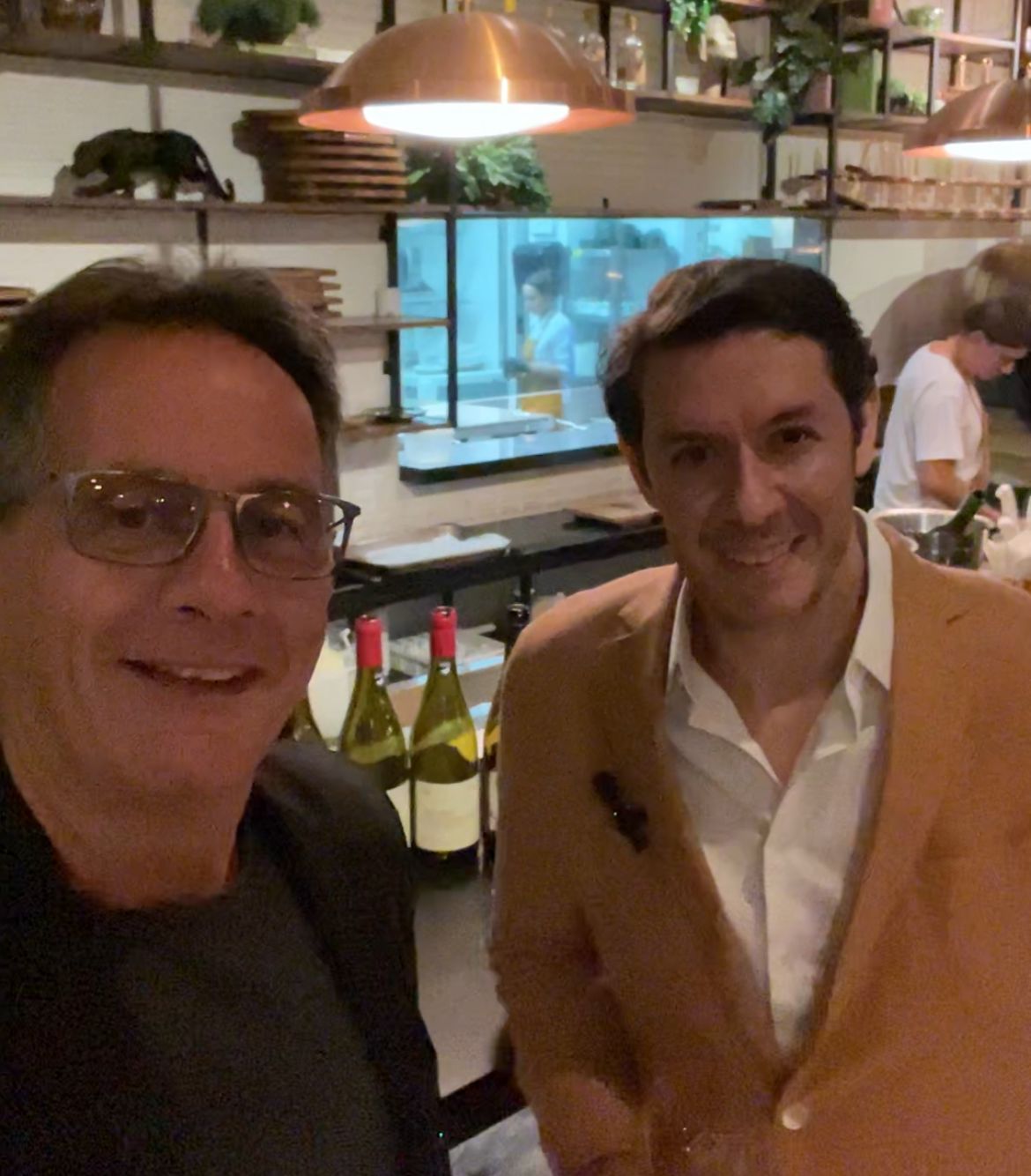 Luis Silveira, on the right, pictured with another guest in a restaurant, with wine bottles behind them.