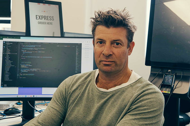 Luke Irving seated at Fingermark with computer screens and ordering technology behind him