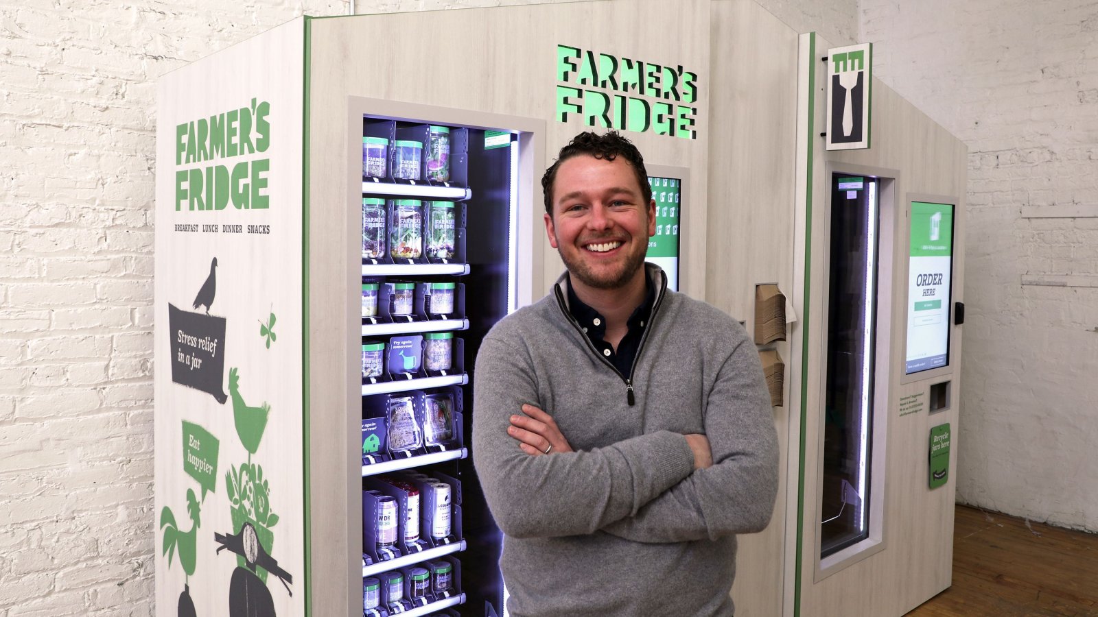 Luke Saunders smiling beside two Farmer's Fridge refrigerated kiosks