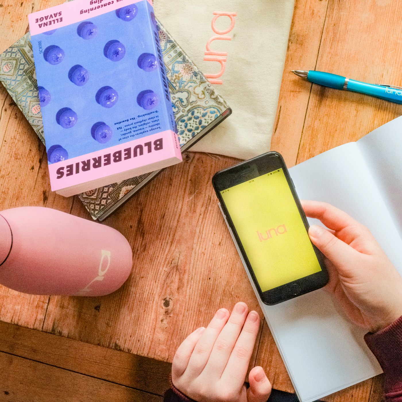 A hand holding a phone displaying the luna app beside a journal and water bottle