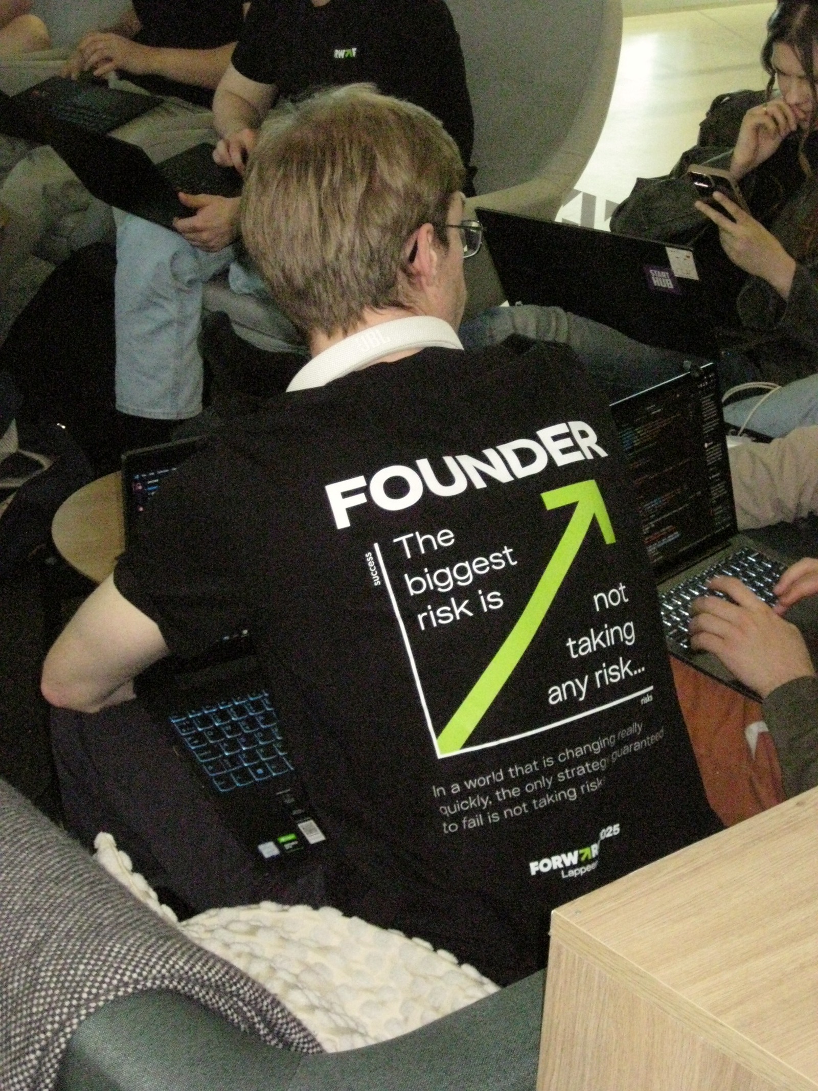 Forward participants working on laptops, with a founder slogan printed on a black T-shirt