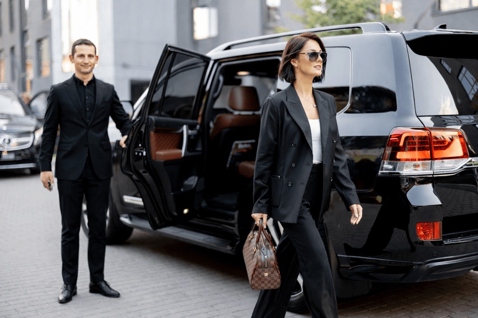 A professional chauffeur holds the door of a black SUV for a business traveler